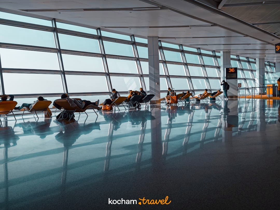 Nowoczesny terminal lotniska, pasażerowie odpoczywający na fotelach przy oknach.