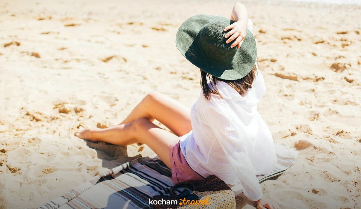 Kobieta w kapeluszu odpoczywająca na słonecznej plaży.