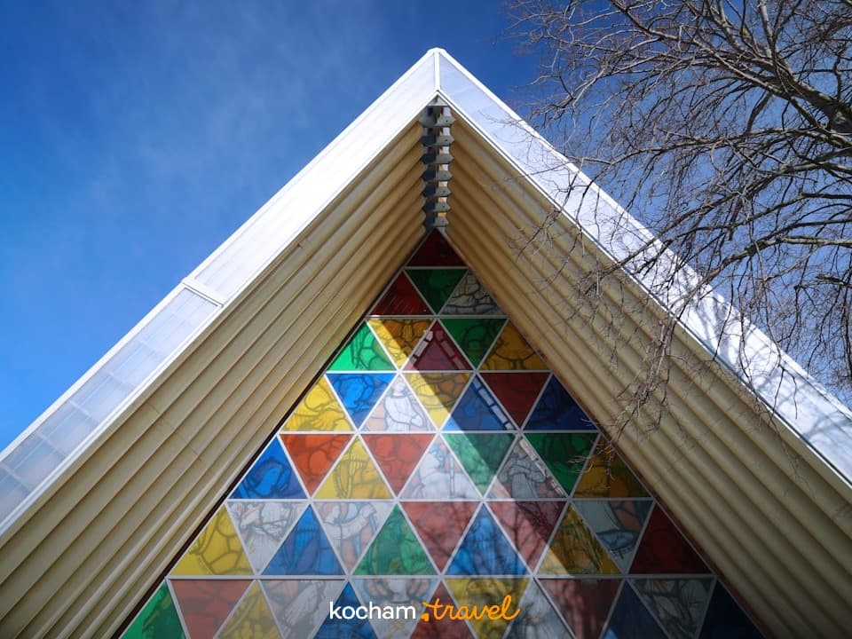 Nowoczesna architektura, trójkątna fasada, kolorowy witraż, błękitne niebo, jasne światło.