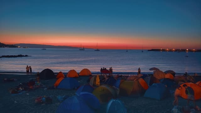 Kolorowy zachód słońca nad plażą pełną namiotów.