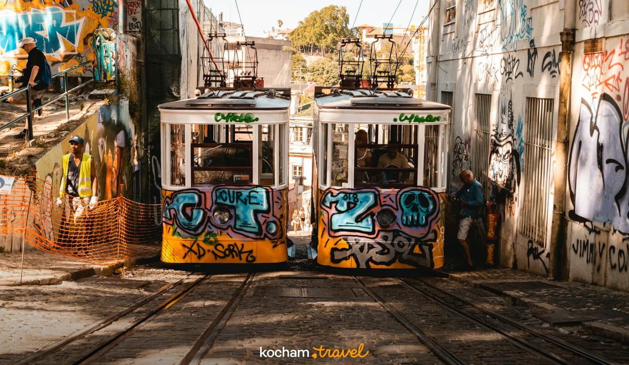 Dwa kolorowe tramwaje z graffiti na torach w słonecznej uliczce.