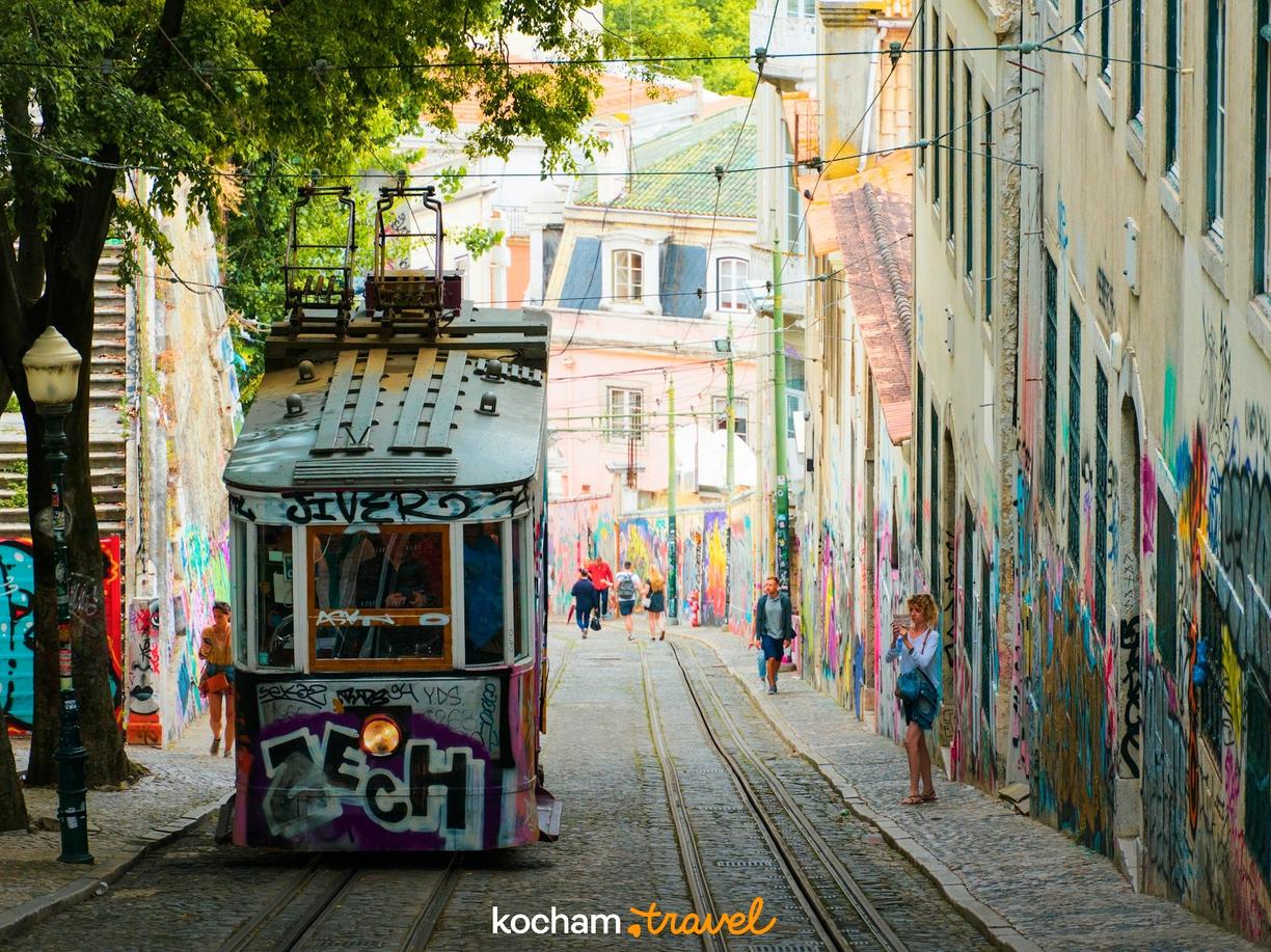 Kolorowy zabytkowy tramwaj w Lizbonie na ulicy pełnej graffiti.