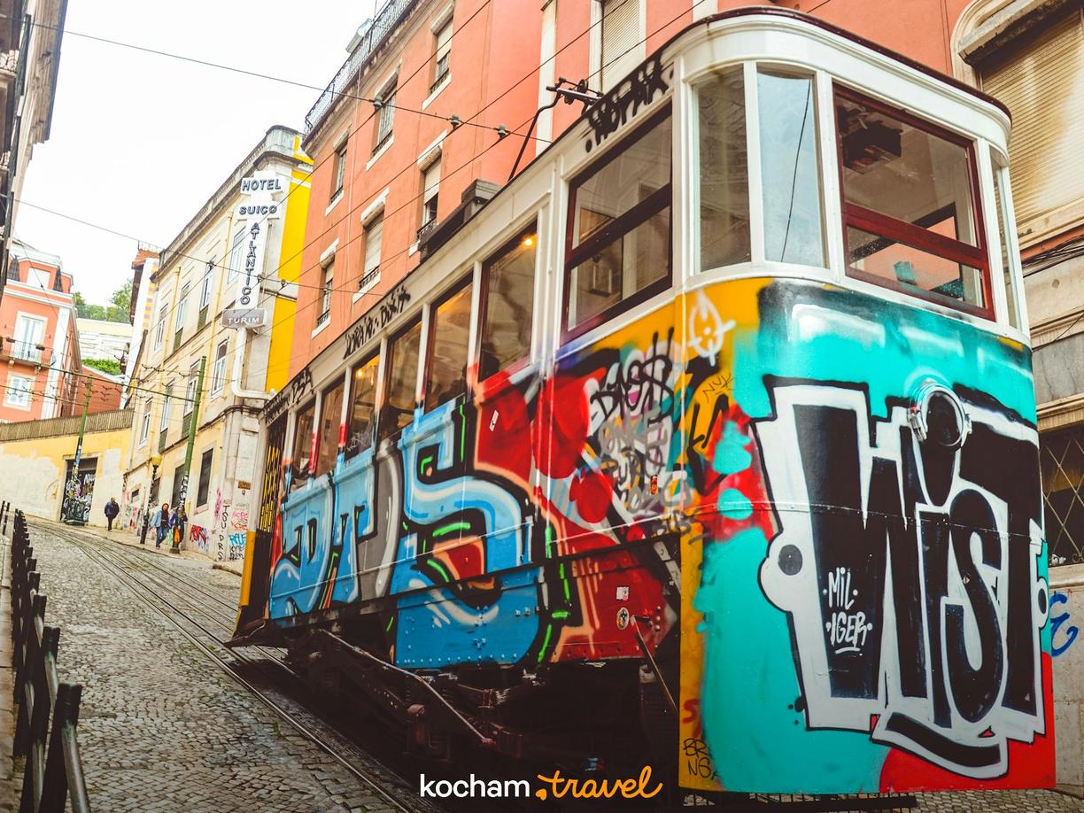 Kolorowy tramwaj z graffiti na stromej, brukowanej ulicy Lizbony.