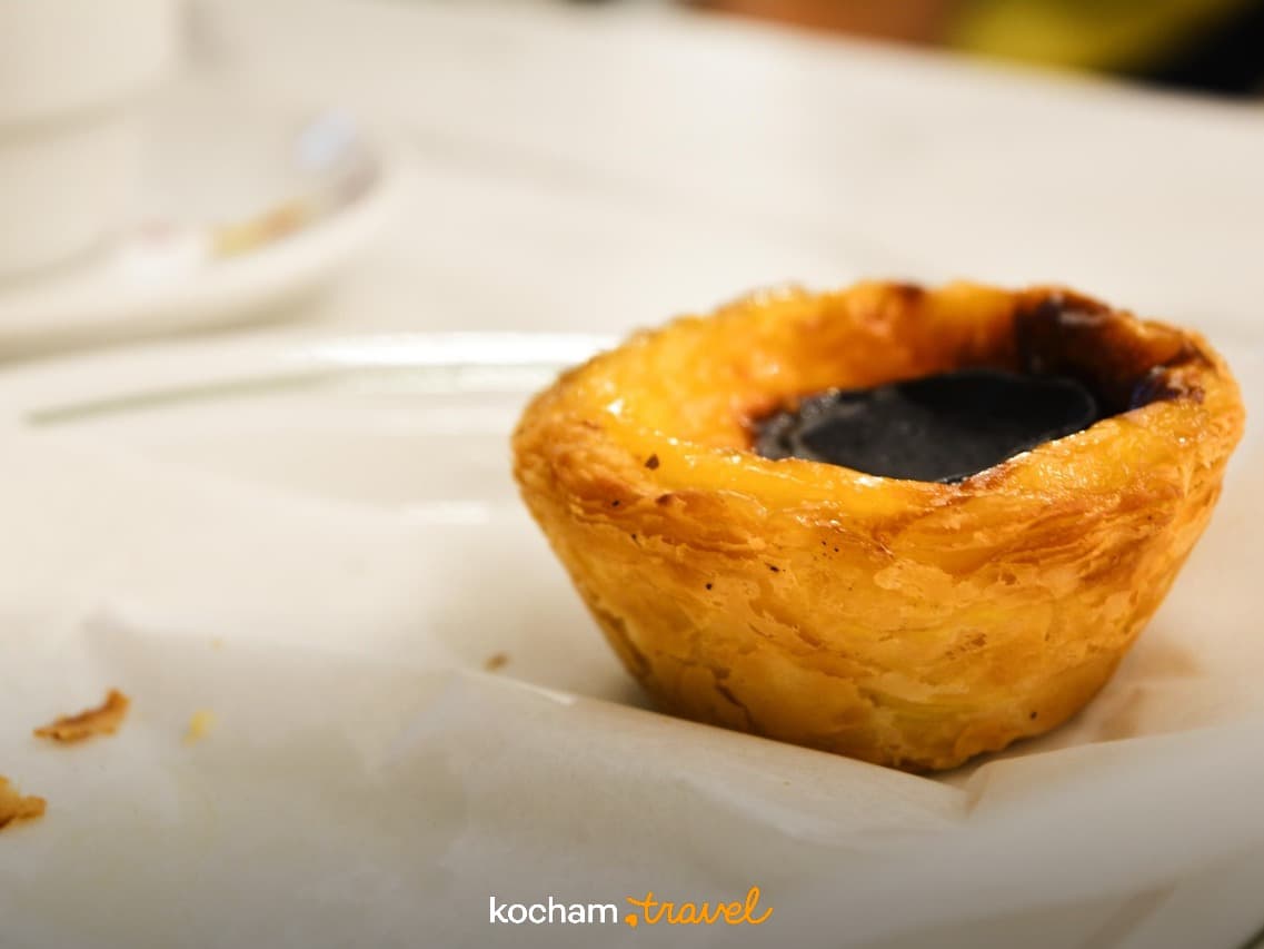 Portugalska tarta jajeczna Pastel de Nata na talerzu, złota skórka, ciemne nadzienie.