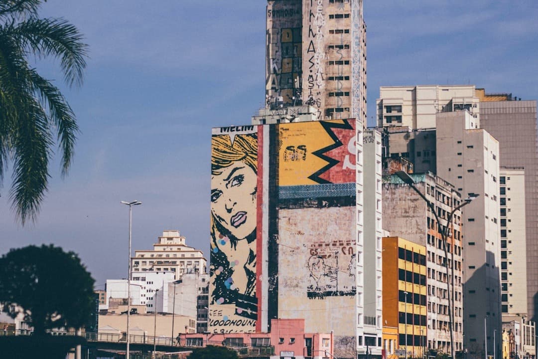 Miasto, budynek z muralem pop-art, sztuka uliczna, palma, błękitne niebo.