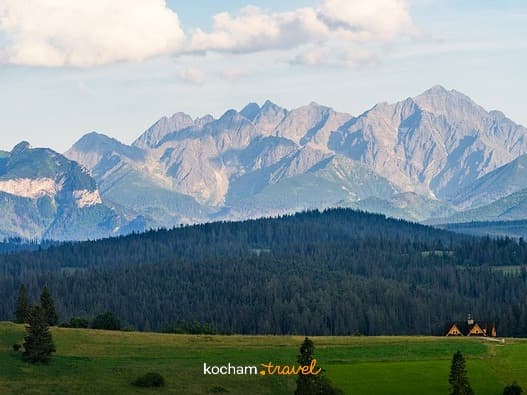 Malowniczy widok Tatr, zielonych pól, lasu i górskiej chaty.