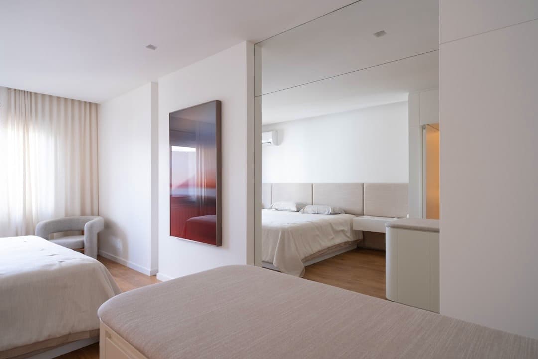 Nowoczesna, minimalistyczna sypialnia hotelowa z dwoma łóżkami i lustrem.