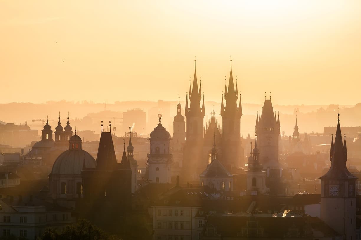 Panorama Pragi o zachodzie słońca, wieże kościołów, zabytkowa architektura.