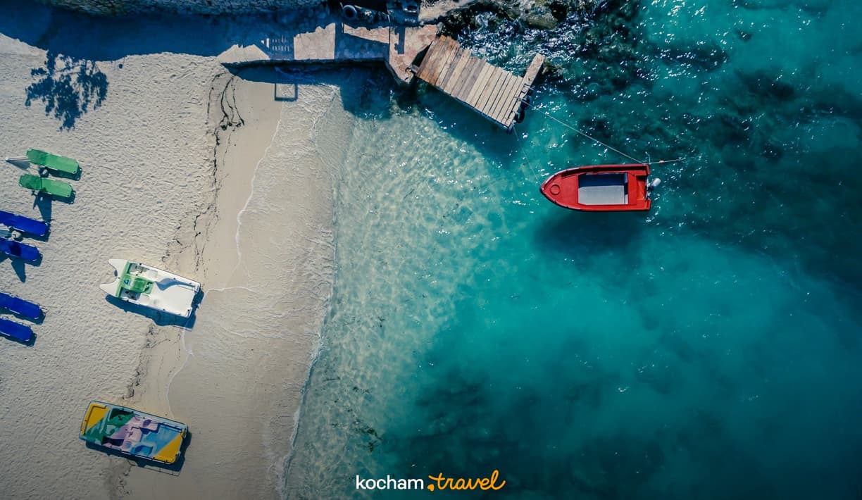 Malownicza plaża z turkusowym morzem, łódką, pomostem i rowerami wodnymi.