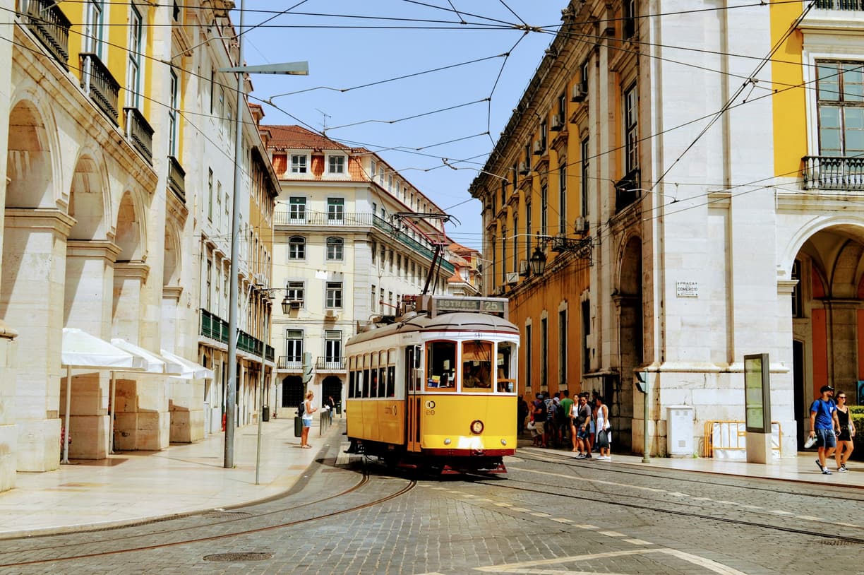 Żółty tramwaj w Lizbonie na brukowanej ulicy wśród zabytkowych kamienic.