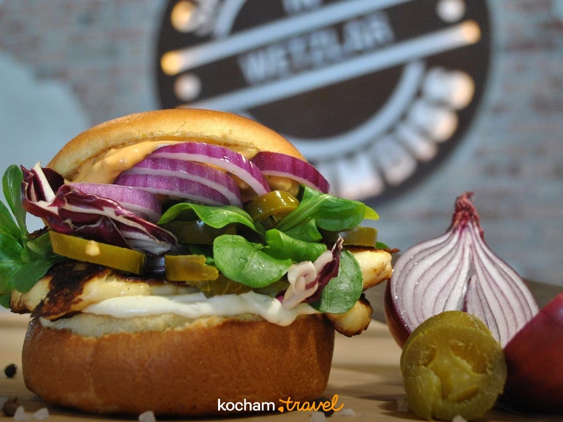 Burger halloumi z czerwoną cebulą, sałatą i piklami na drewnianej desce.