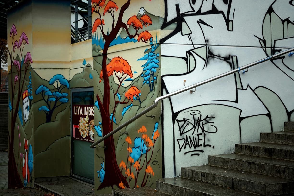 Miejski mural z drzewami, lisem i graffiti na ścianie budynku ze schodami.