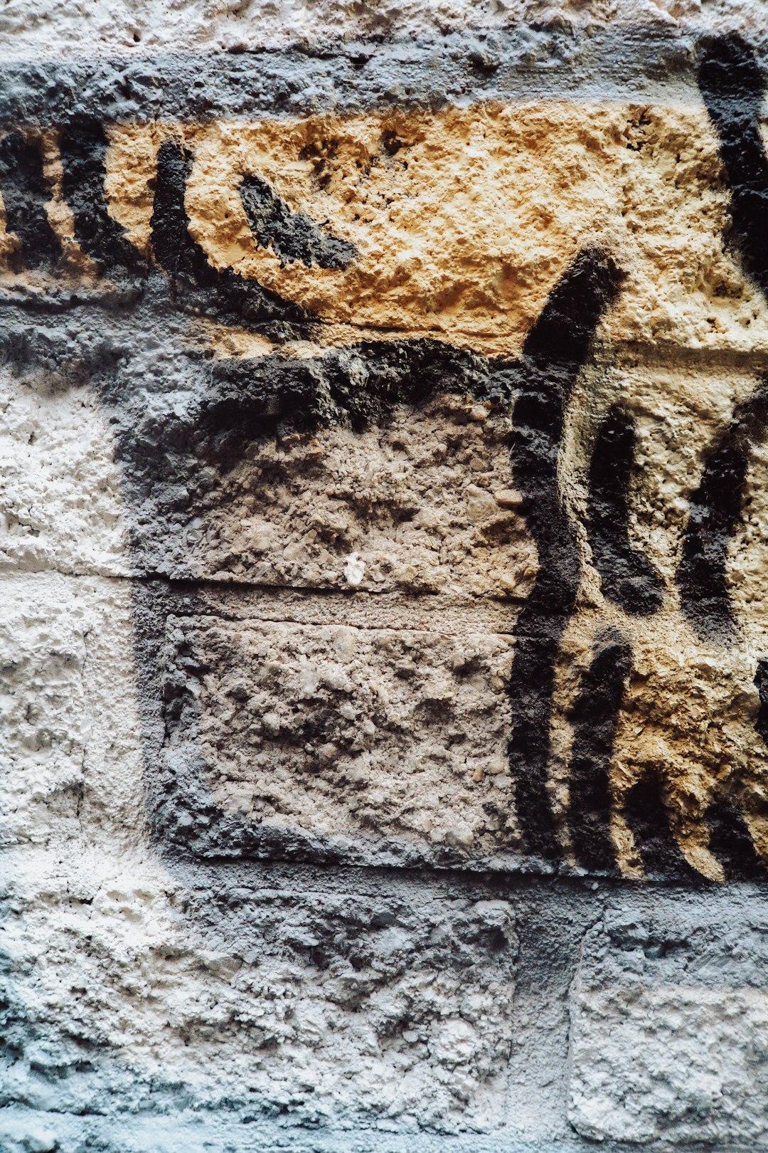 Szorstki mur z abstrakcyjnym graffiti w odcieniach szarości i beżu.