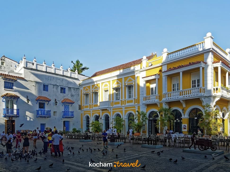 Tętniący życiem kolonialny plac Cartagena, żółte budynki, ludzie, gołębie.