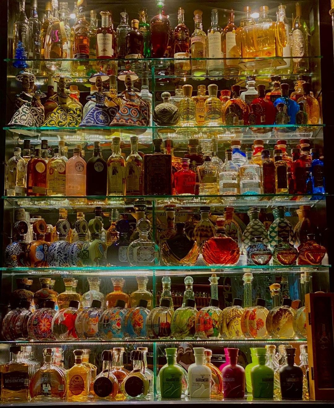 Kolekcja kolorowych butelek tequili na półkach.