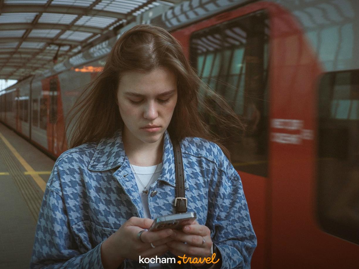 Podróżująca kobieta na peronie sprawdza telefon, pociąg przejeżdża.