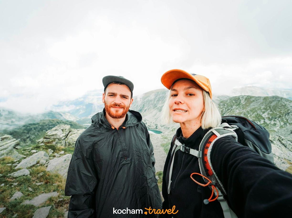Para wędrowców robi selfie w górach z widokiem na jezioro.