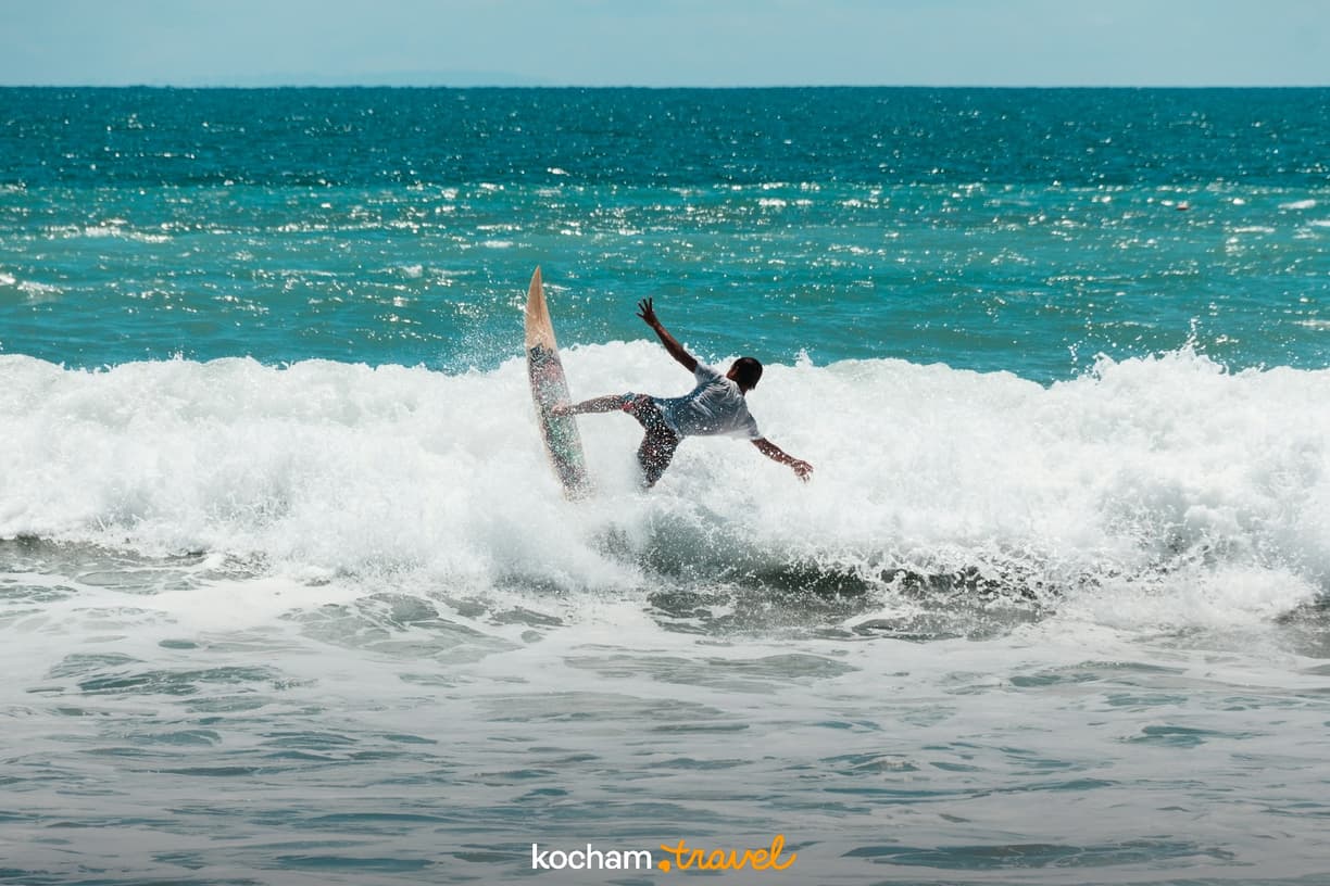 Surfer balansujący na szczycie spienionej fali w błękitnym oceanie.