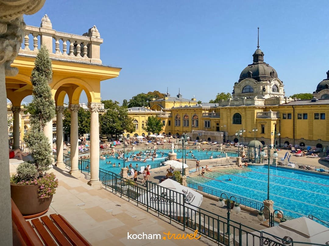 Szechenyi Termy Budapeszt, żółty budynek, baseny zewnętrzne, kąpiący się ludzie.