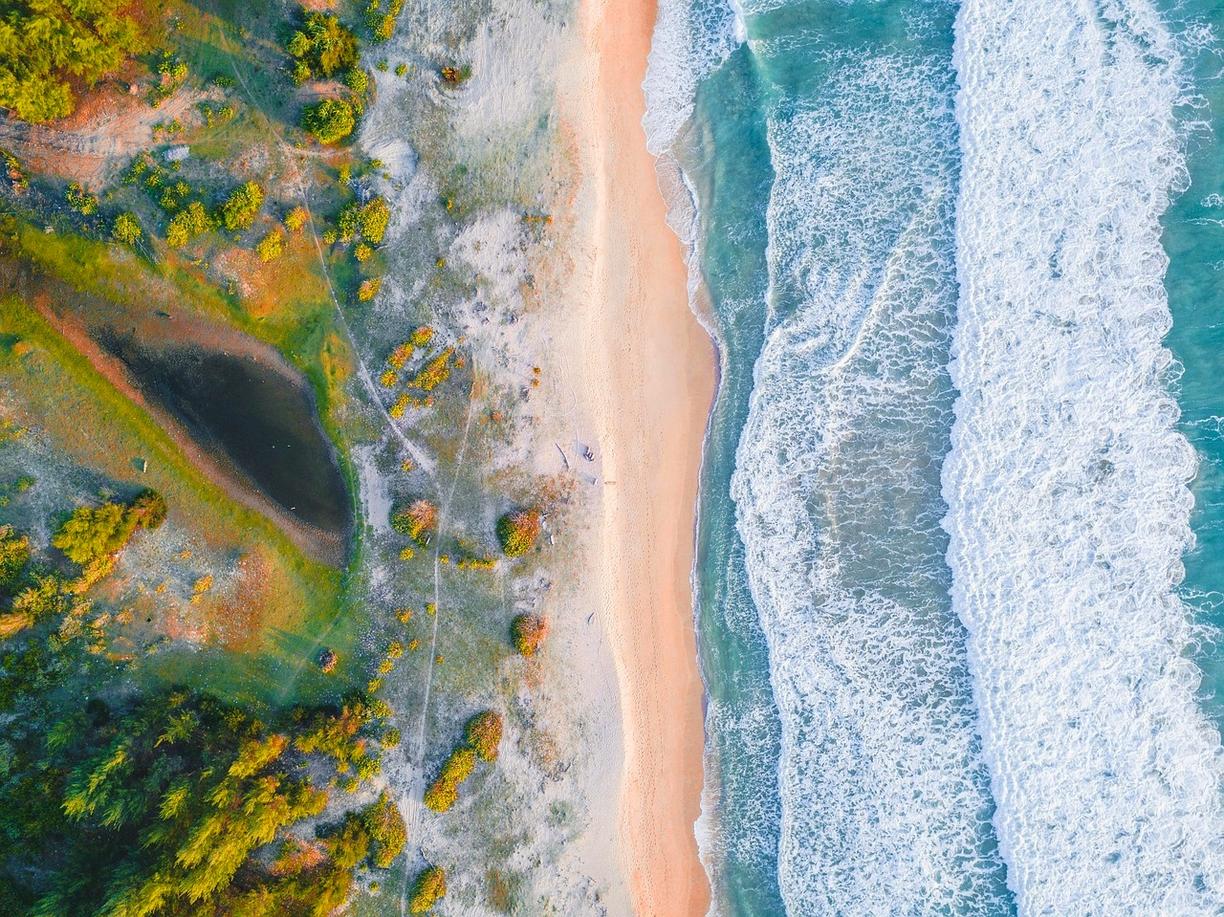 Panoramiczny widok plaży, turkusowych fal oceanu i zielonego wybrzeża.