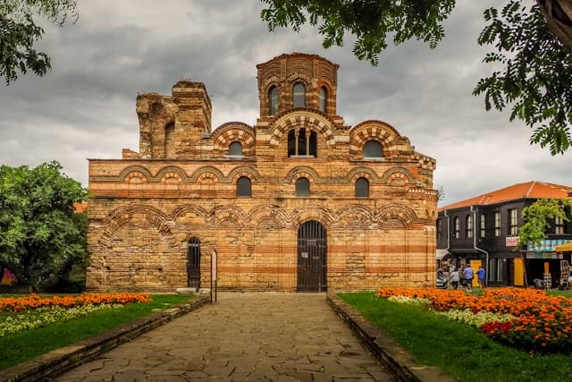 Zabytkowa ceglana cerkiew Chrystusa Pantokratora w Nesebyrze wśród kwiatów.
