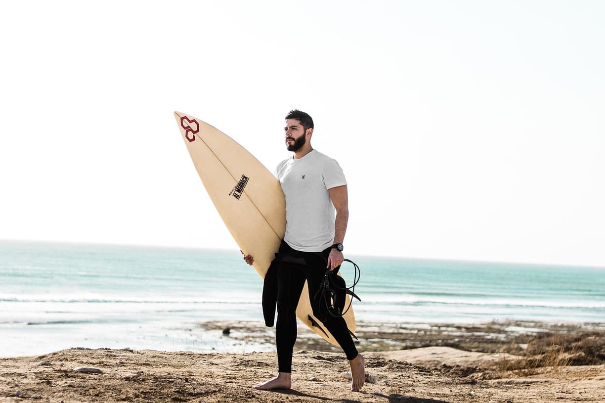 Mężczyzna z deską surfingową i pianką na piaszczystej plaży.