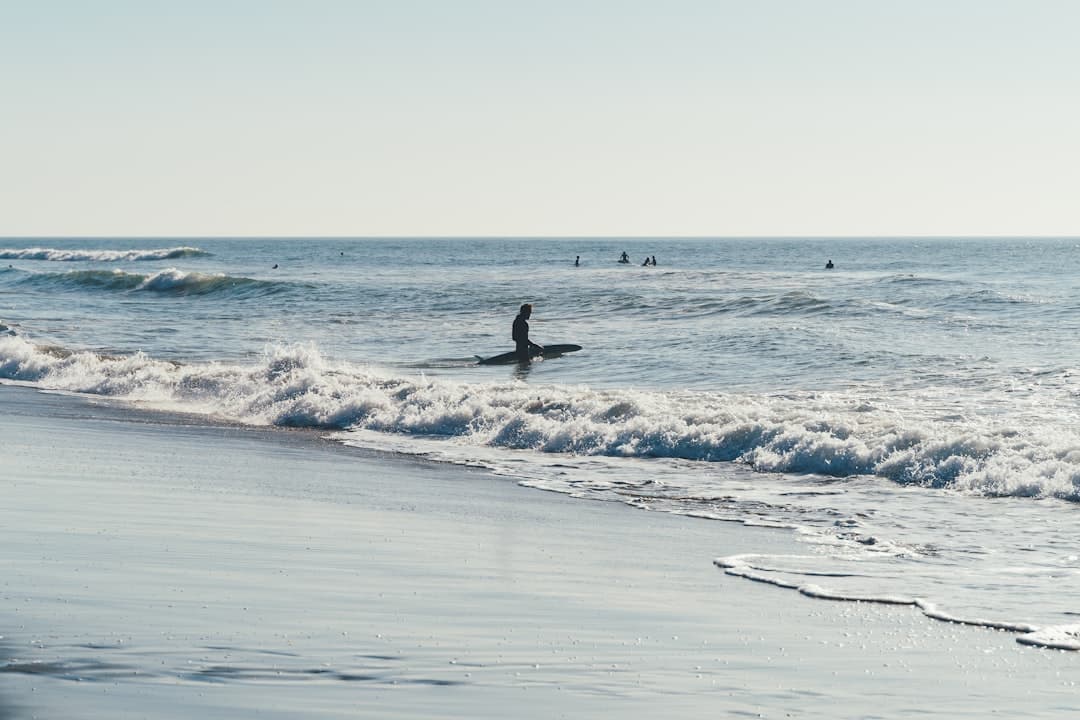 Surfer na desce w oceanie, z falami i innymi surferami w tle.