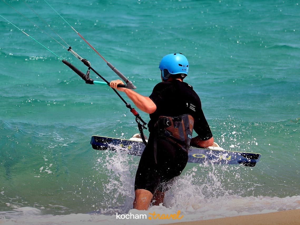 Kitesurfer w turkusowym morzu z deską na słonecznej plaży.