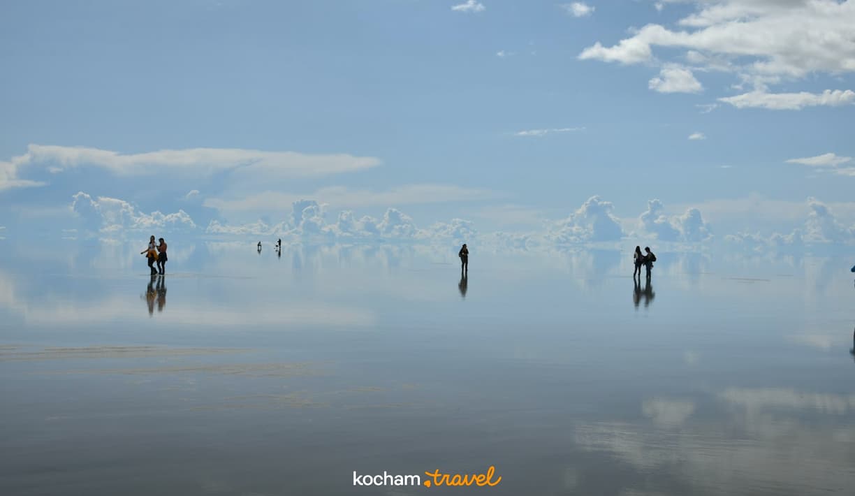Turyści na solnisku Salar de Uyuni z idealnym odbiciem nieba.