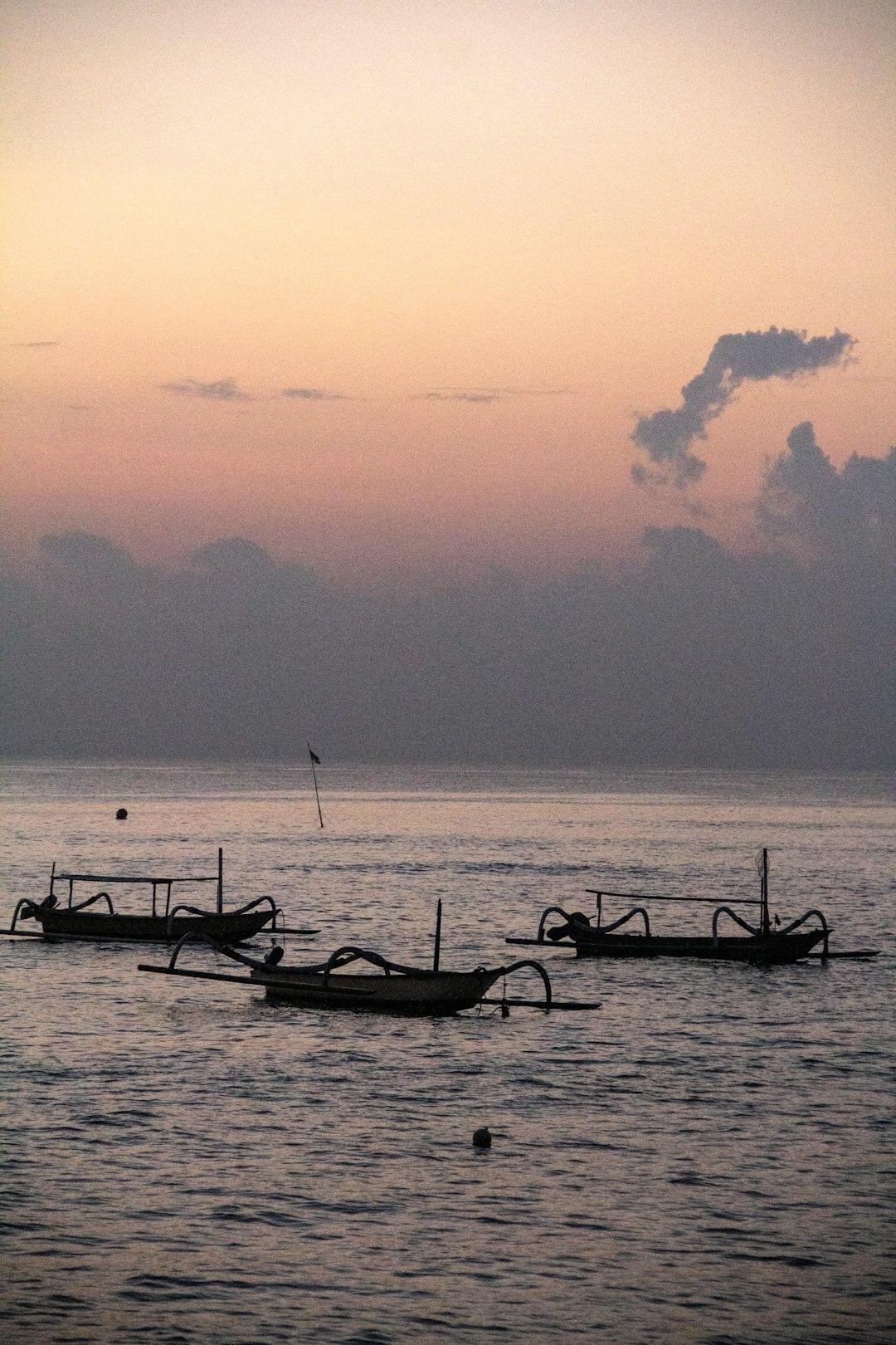 Sylwetki tradycyjnych łodzi rybackich na spokojnej wodzie o świcie.