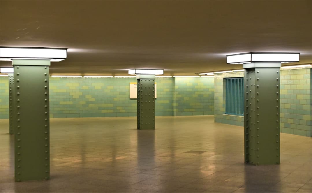Podziemny korytarz, zielone ściany, filary, oświetlenie.