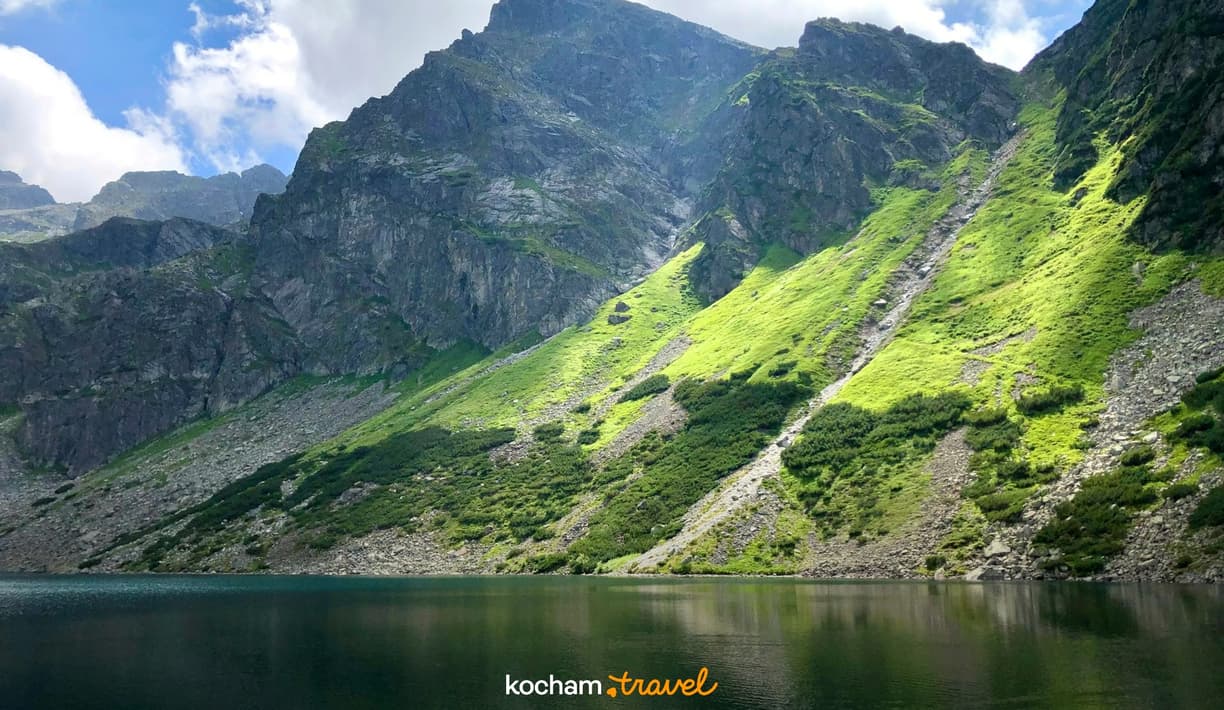 Jezioro górskie w Tatrach z zielonymi, nasłonecznionymi zboczami.
