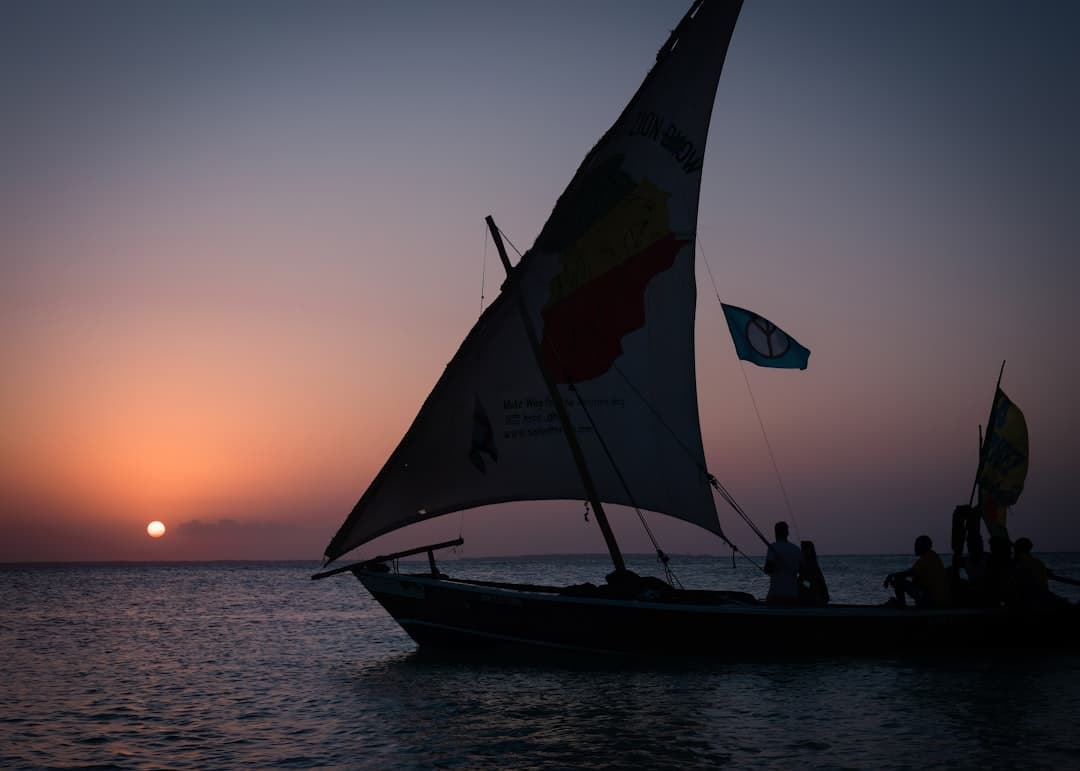 Tradycyjny dhow z ludźmi na pokładzie podczas zachodu słońca nad oceanem.