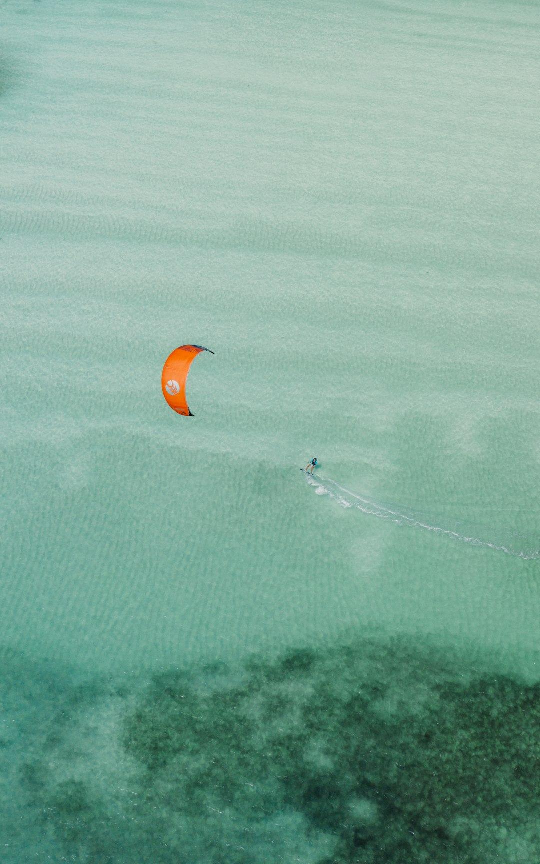Kitesurfer na turkusowej wodzie z pomarańczowym latawcem.