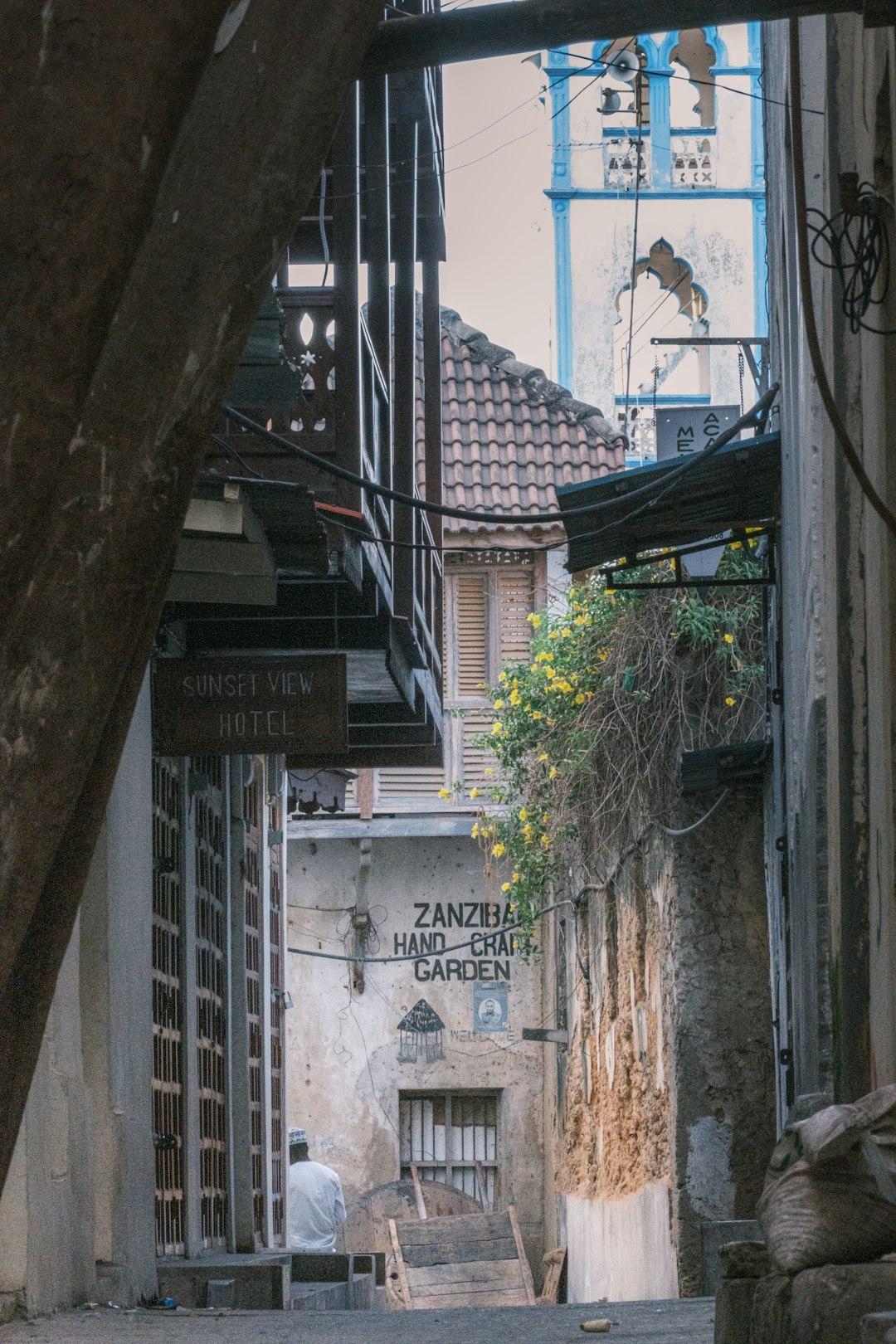 Uliczka Zanzibaru z siedzącym człowiekiem, hotelem i minaretem w tle.