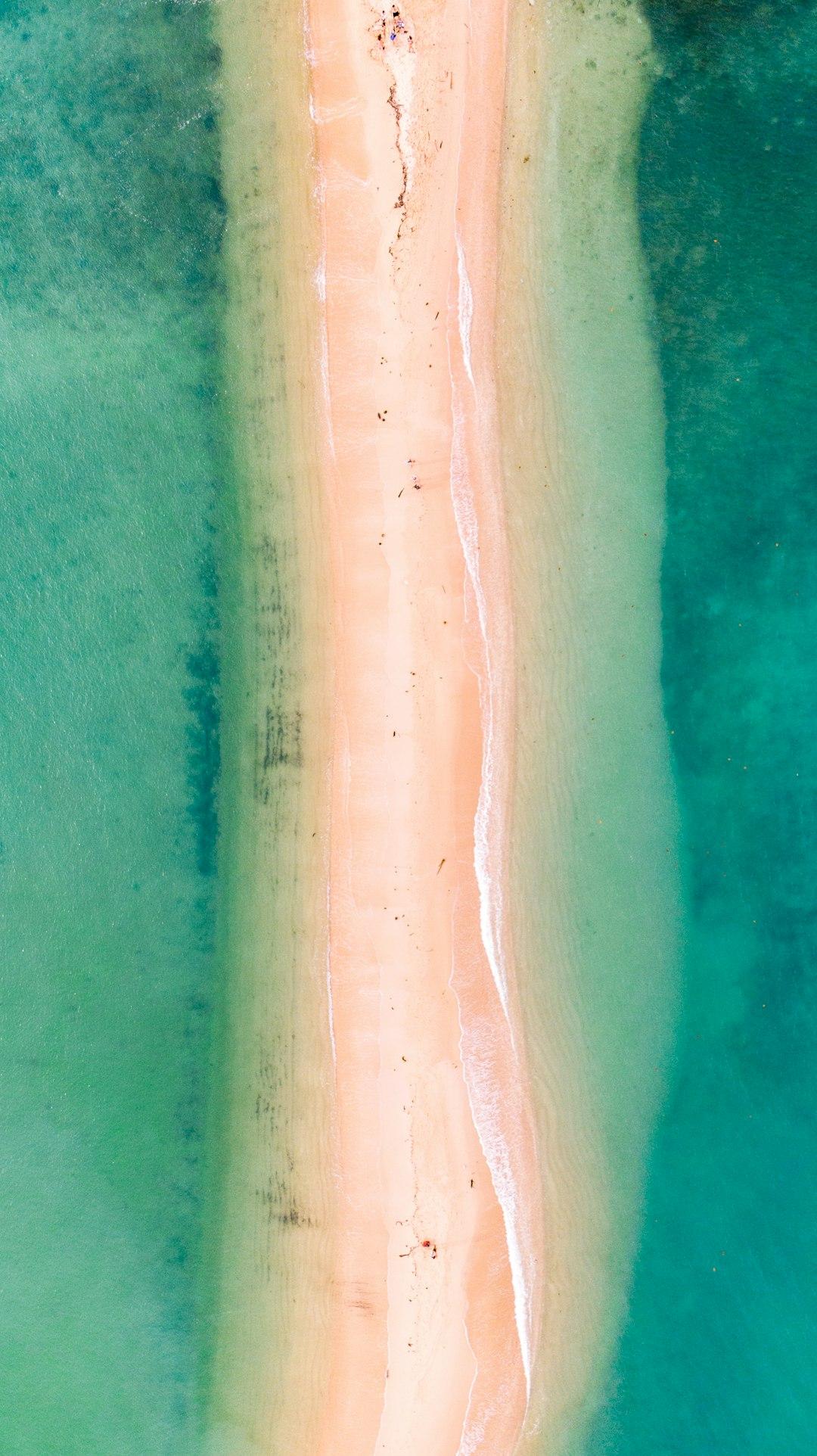 Wąska piaszczysta ławica otoczona turkusowym oceanem z falami.