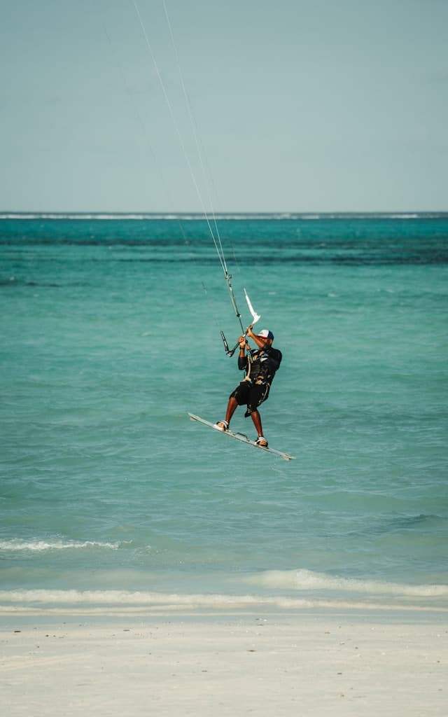 Kitesurfer wykonujący skok nad turkusową wodą oceanu przy plaży.