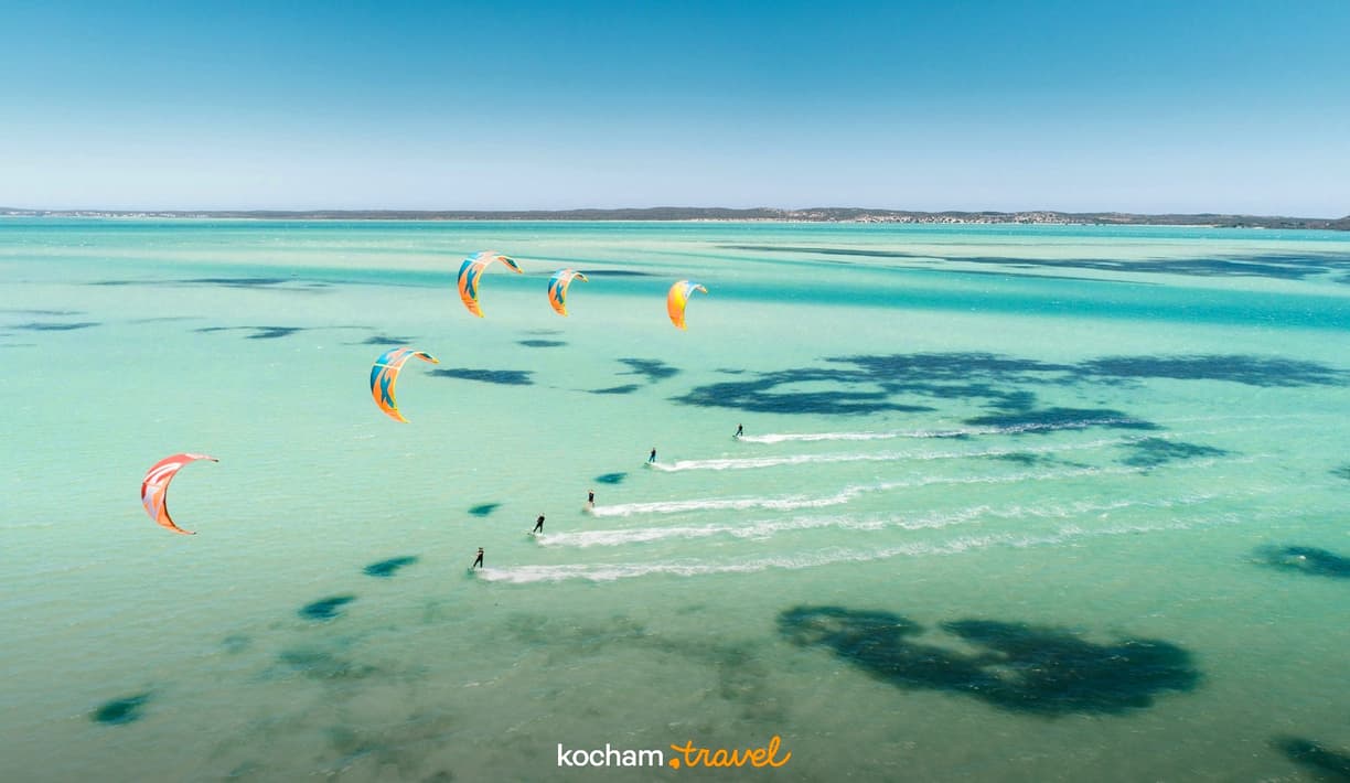Kitesurferzy na czystej, turkusowej wodzie pod błękitnym niebem.