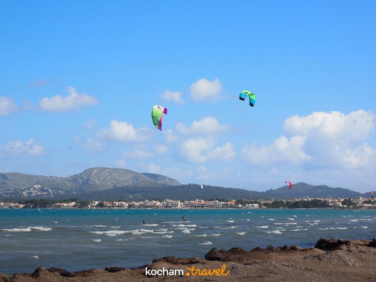 Kitesurfing na turkusowej zatoce, góry i miasto w tle.