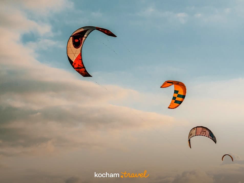 Wielobarwne latawce kitesurfingowe szybujące na tle zachmurzonego nieba.