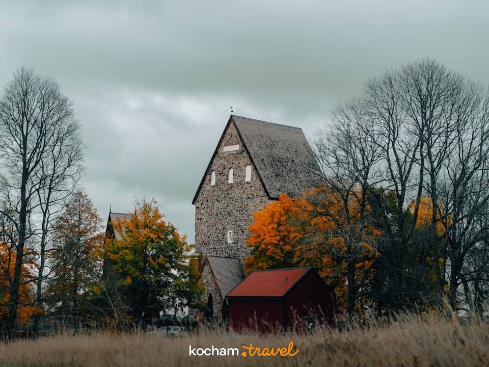 Historyczny kamienny kościół, jesienne drzewa, pochmurne niebo, wiejski krajobraz.