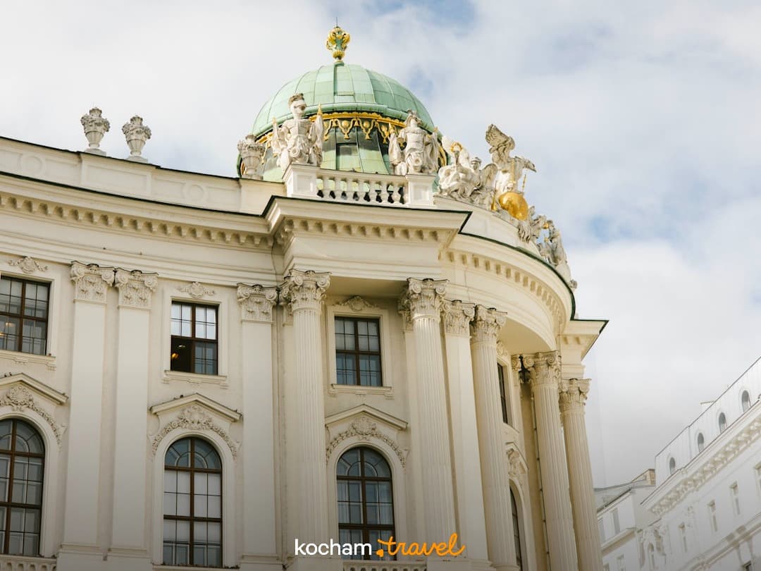 Ozdobny klasyczny budynek z zieloną kopułą i złotymi rzeźbami.