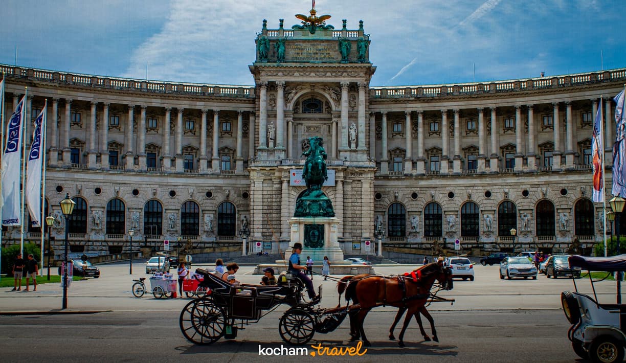 Wiedeński fiaker z turystami przed Pałacem Hofburg w słoneczny dzień.