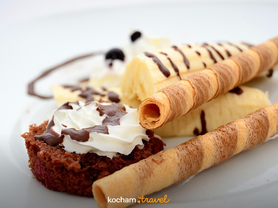 Pyszny deser z ciastem czekoladowym, bitą śmietaną, bananami i rurkami waflowymi.