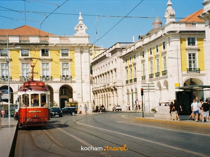 Klasyczny czerwony tramwaj w Lizbonie, zabytkowe budynki, słoneczny dzień.