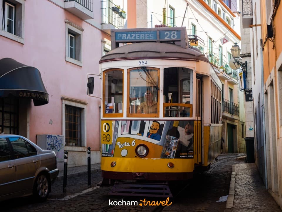 Żółty zabytkowy tramwaj linii 28 na brukowanej ulicy Lizbony.