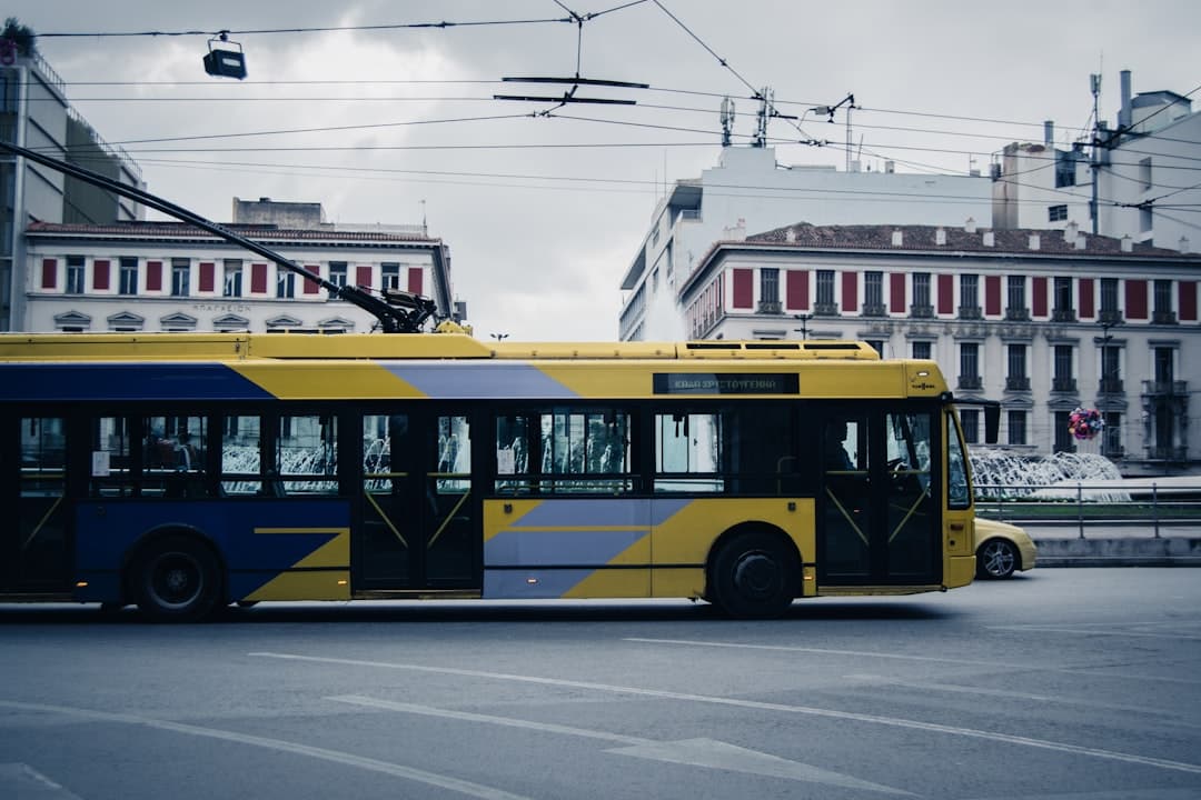Żółto-niebieski trolejbus na tle miejskiego budynku.