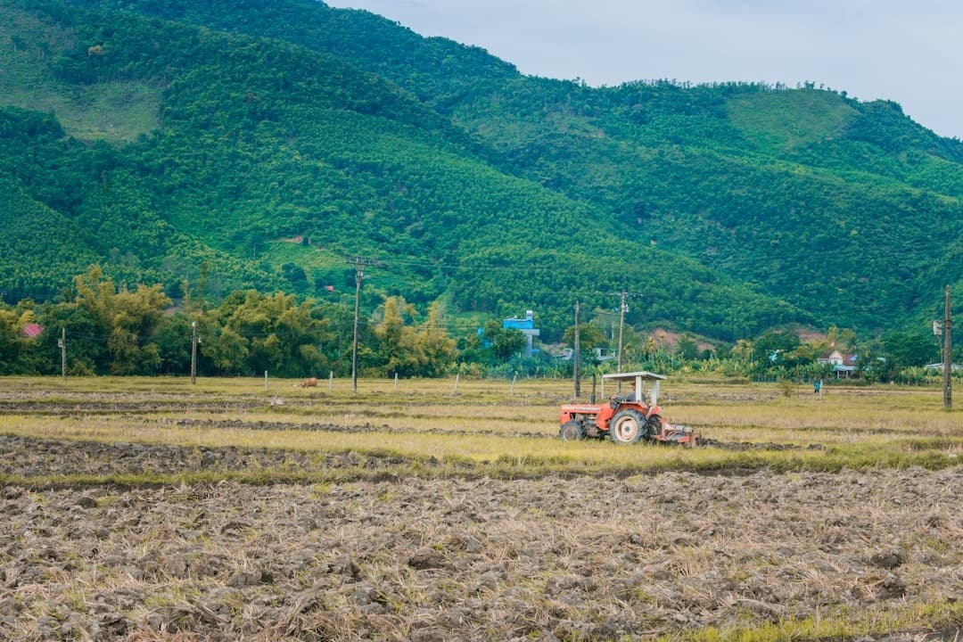 Pomarańczowy traktor na zaoranym polu, zielone góry, wiejski krajobraz.