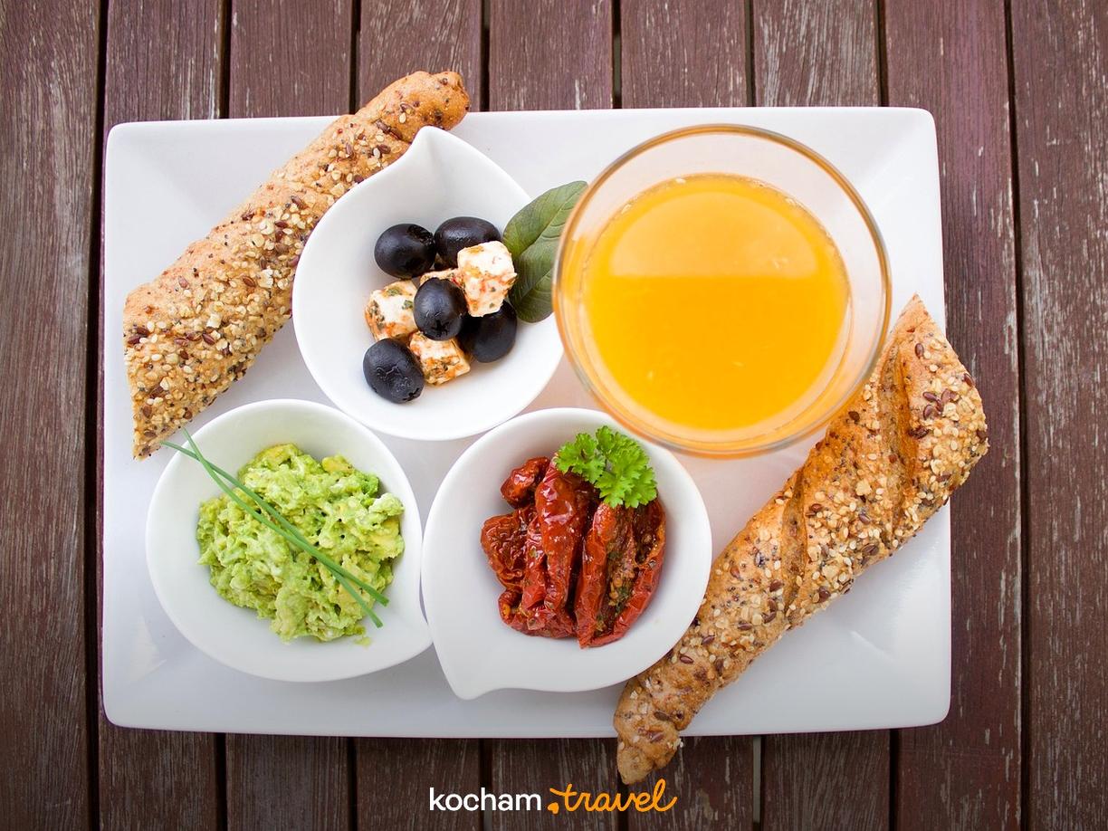 Zdrowe śniadanie: bagietki, oliwki, guacamole, suszone pomidory i sok pomarańczowy.