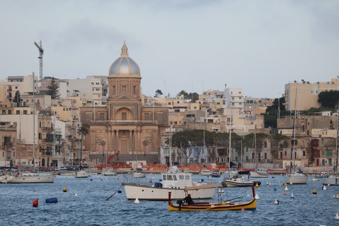 Maltański port z historycznym kościołem kopułowym i tradycyjnymi łodziami na wodzie.